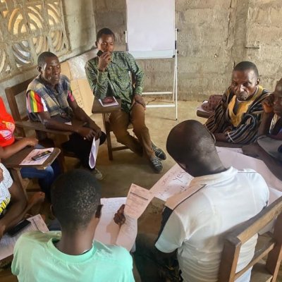 Group of people sitting in a circle, reviewing documents in a workshop in Liberia.