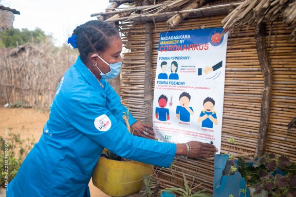 Photo of a woman in a USAID jumpsuit putting up a Covid-19 poster in Madagascar