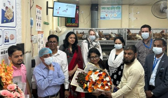 People with flowers standing in front of bird cages at a market