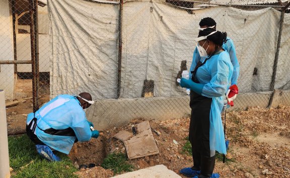 Three people in PPE sampling wastewater outside a hospital.