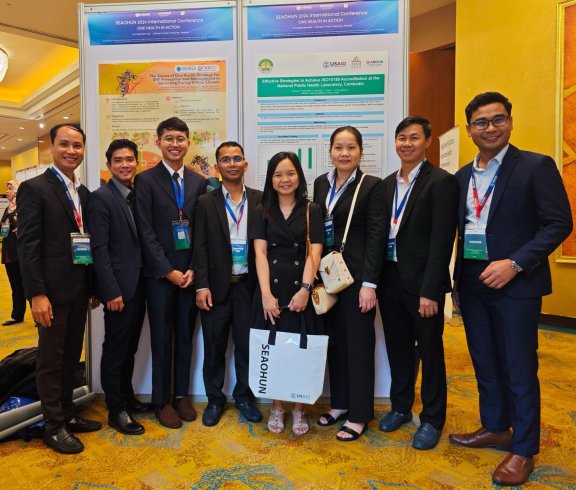 Group photo at the conference lobby, in front of the presentation poster.