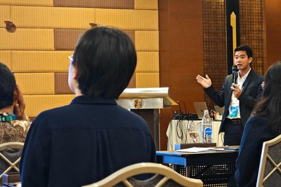 Mr. Chhan talking into a microphone and answering a question, as participants look at the presentation.