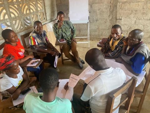 Group of people sitting in a circle, reviewing documents in a workshop in Liberia.